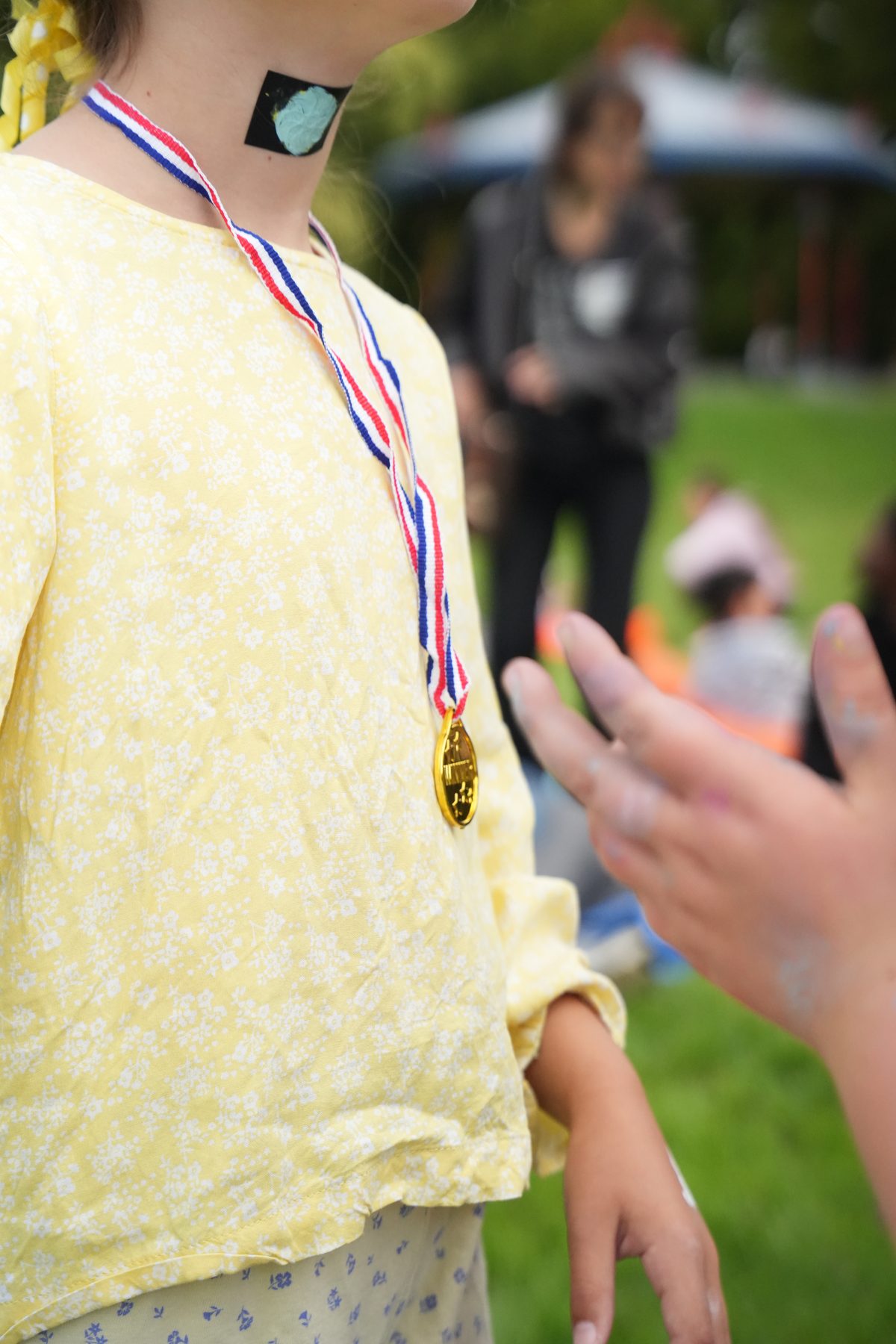 A child in a yellow floral top wearing a gold Winner medal on a red, white and blue ribbon